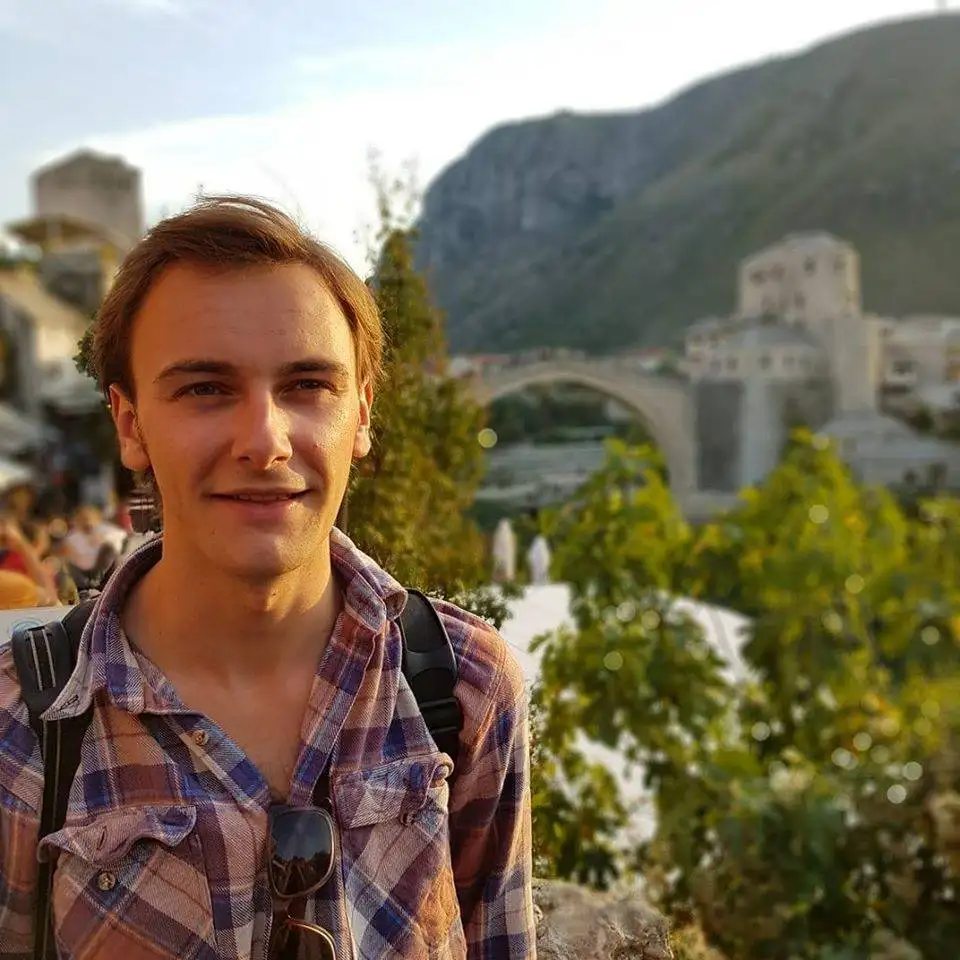 a young man standing in front of a bridge.