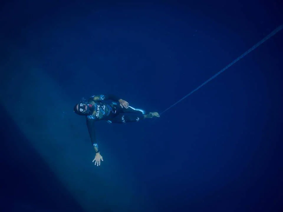 a scuba diver in a wetsuit hanging from a rope.