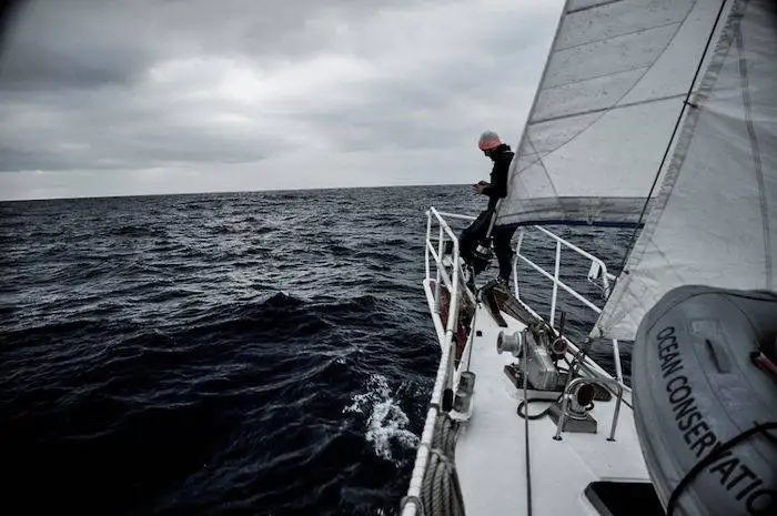 a man is standing on the bow of a sailboat in the ocean.