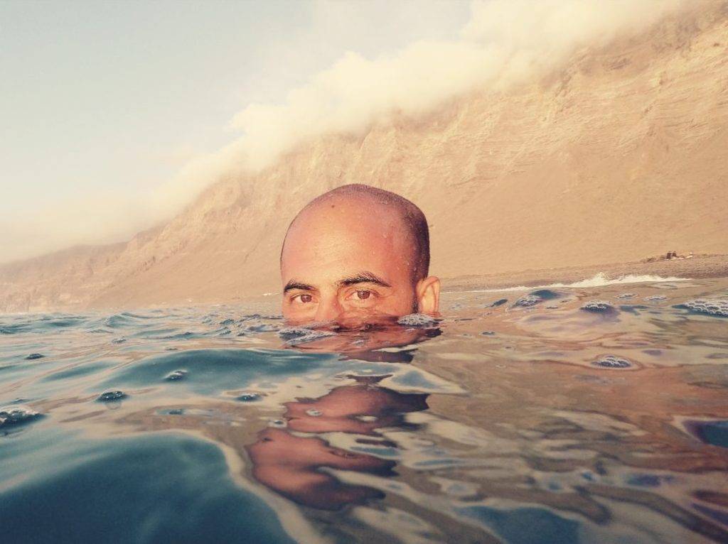 a man swimming in the ocean with a mountain in the background.