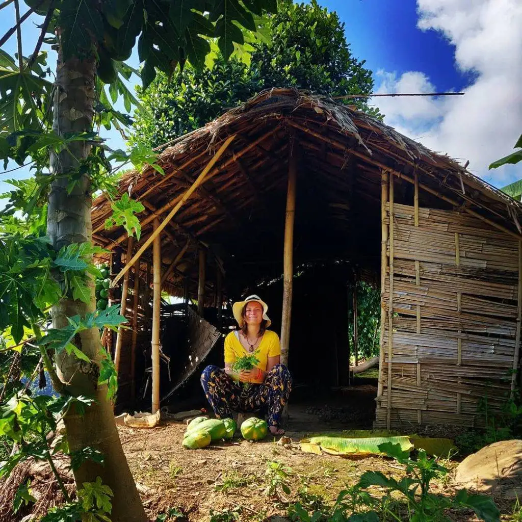 a woman sitting in front of a hut.