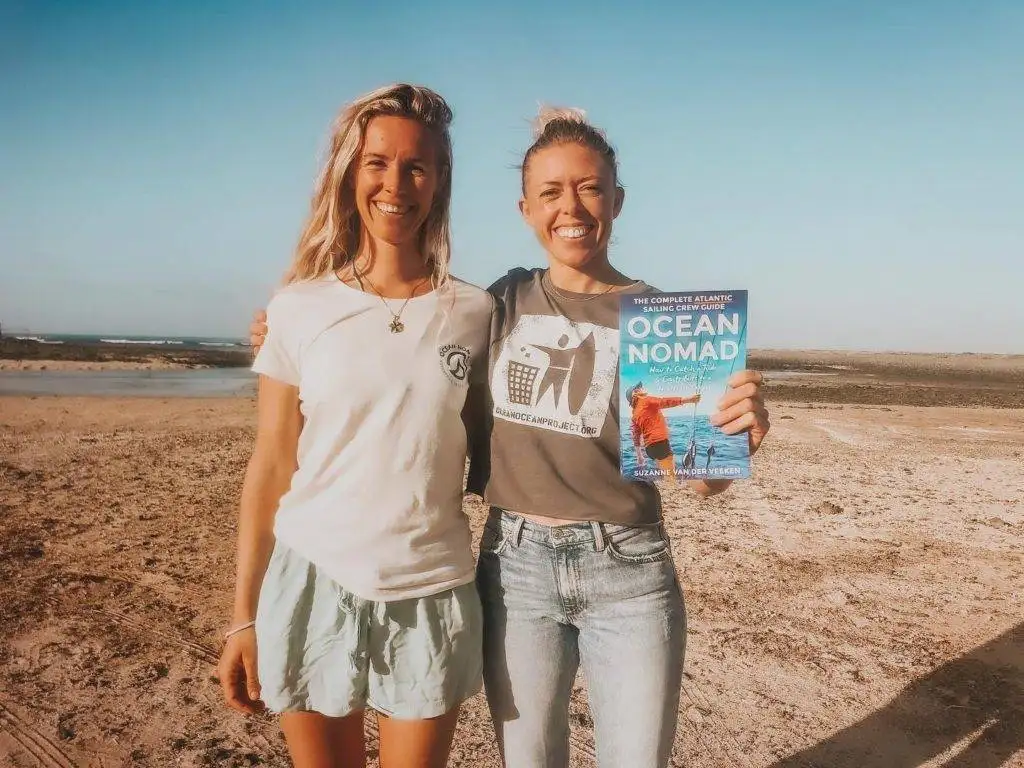 two women standing on a beach with a book in their hands.