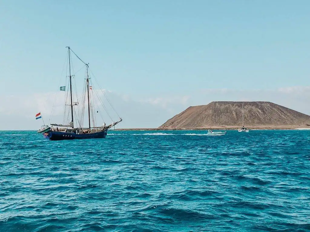 a sailboat is sailing in the ocean near a mountain.