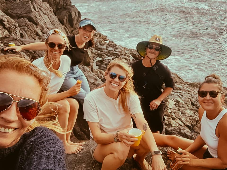 a group of women posing for a photo on a rocky beach.