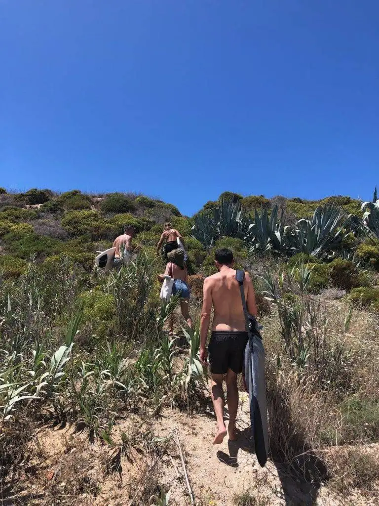 a group of people walking up a hill with a surfboard.