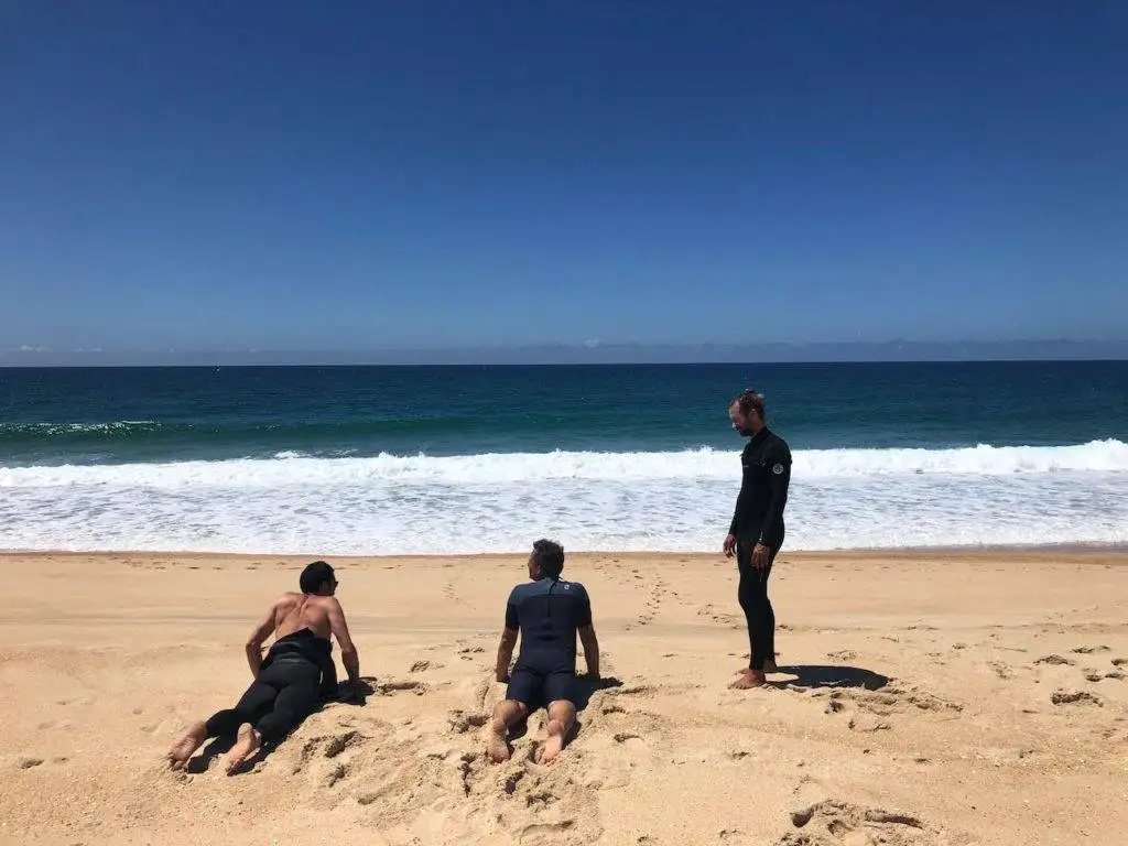 three men sitting on the sand in front of the ocean.