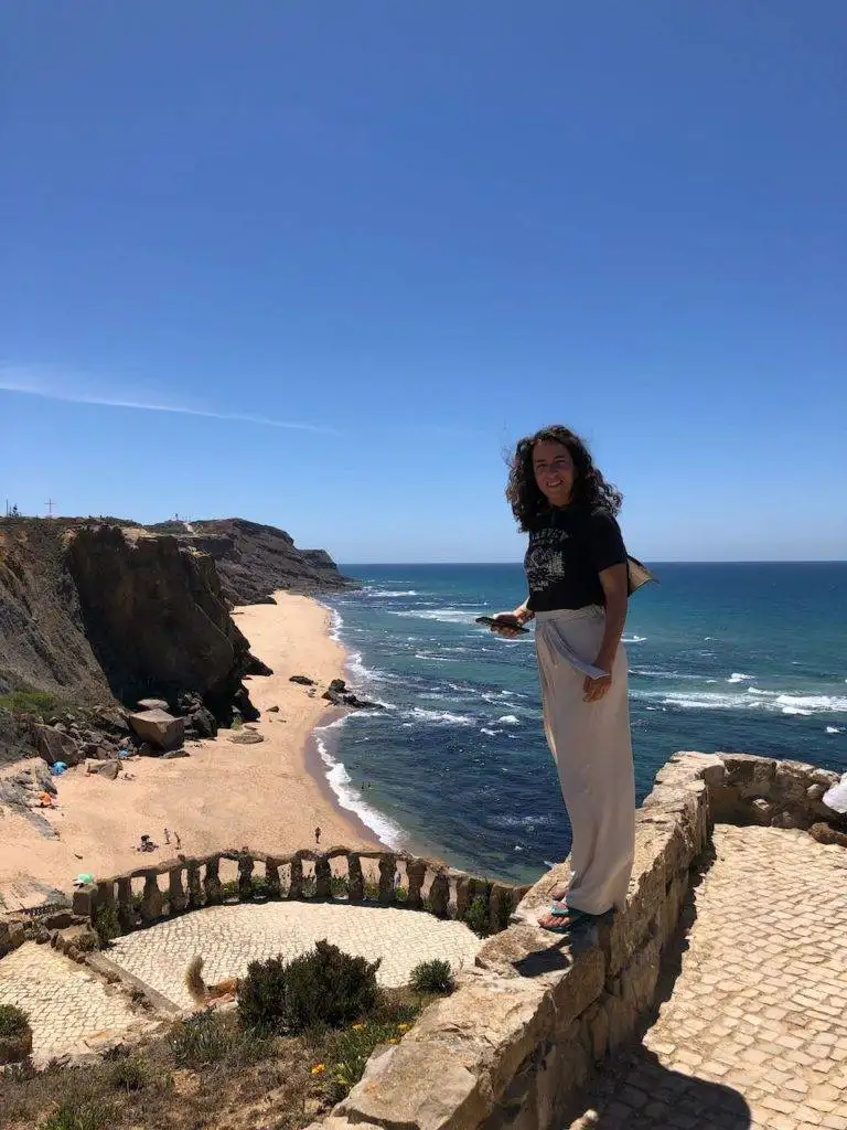 a woman standing on a stone wall near the ocean.
