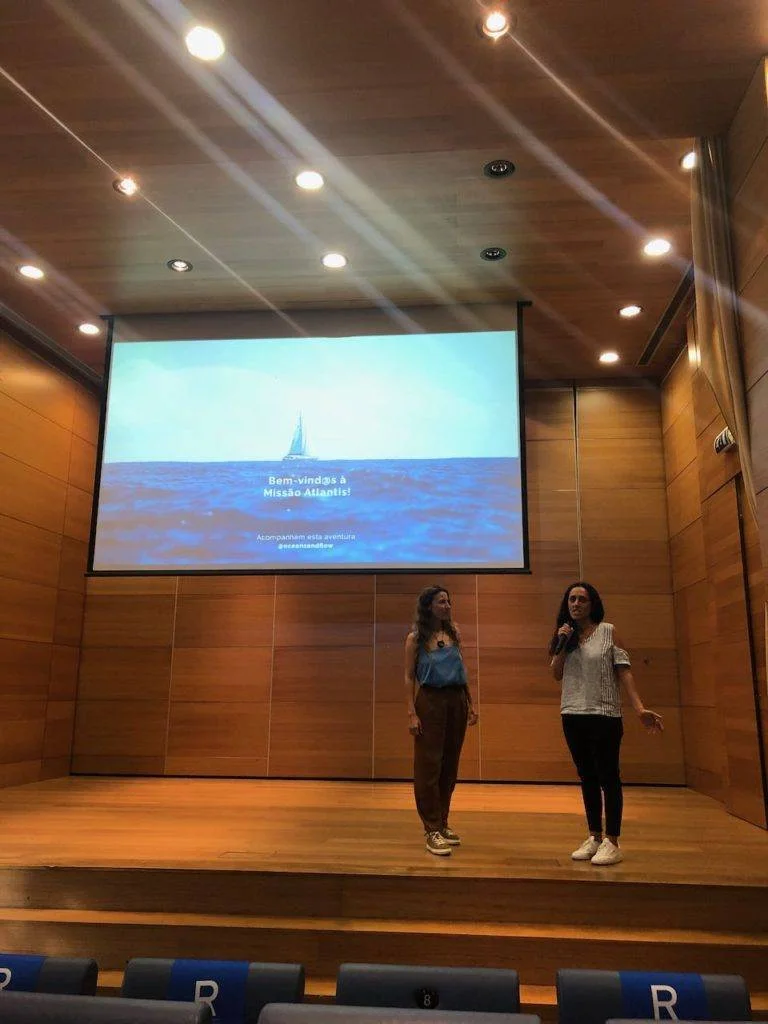two women standing on stage in front of a projection screen.
