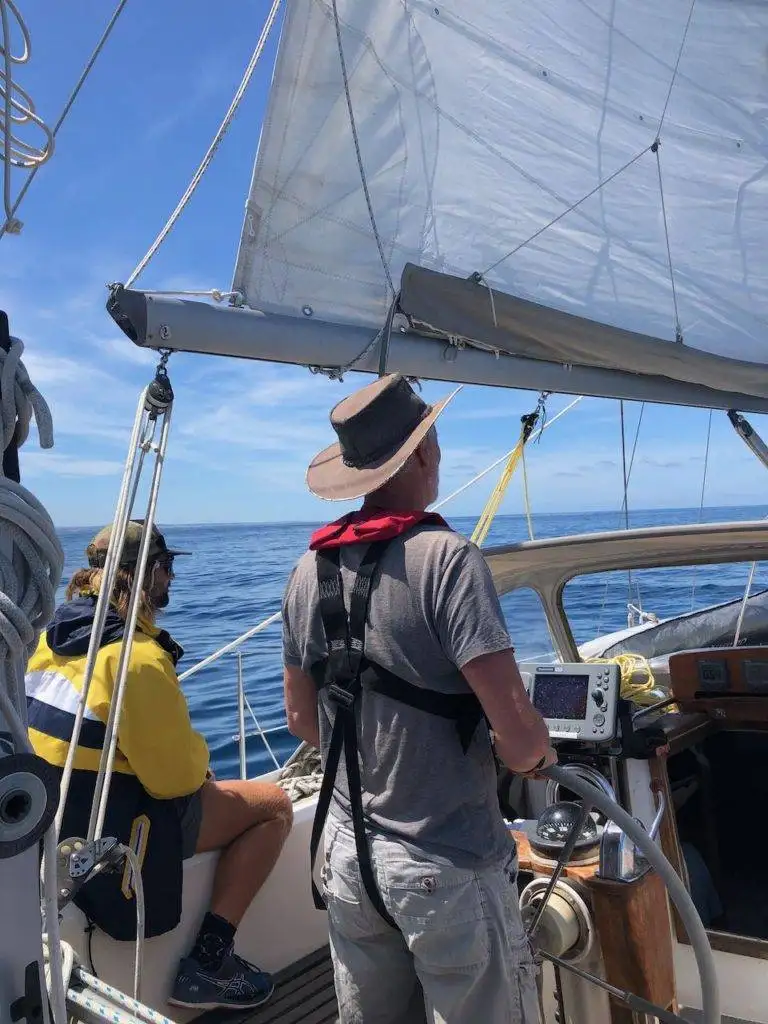 a man is standing on the deck of a sailboat.