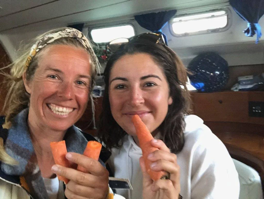 two women sitting on a boat eating carrots.