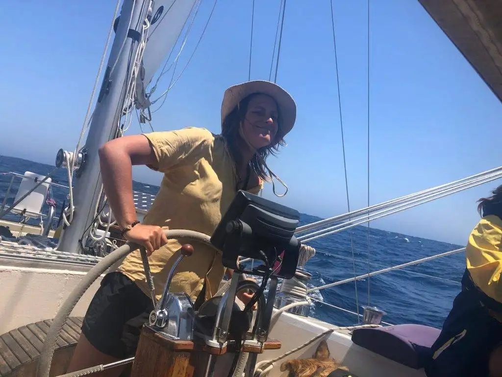 a woman in a yellow hat is standing on the deck of a sailboat.