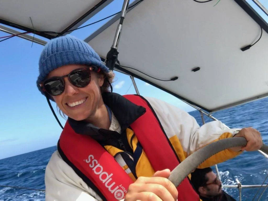 a man wearing a hat and sunglasses is steering a sailboat.