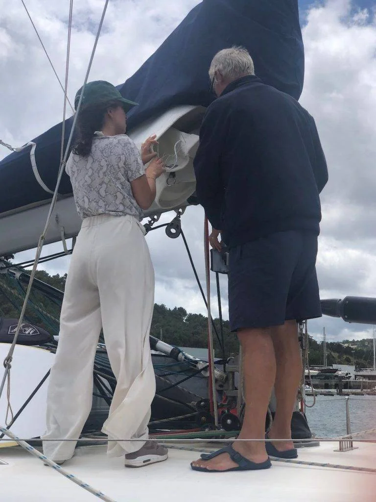 a man and woman standing on the bow of a sailboat.