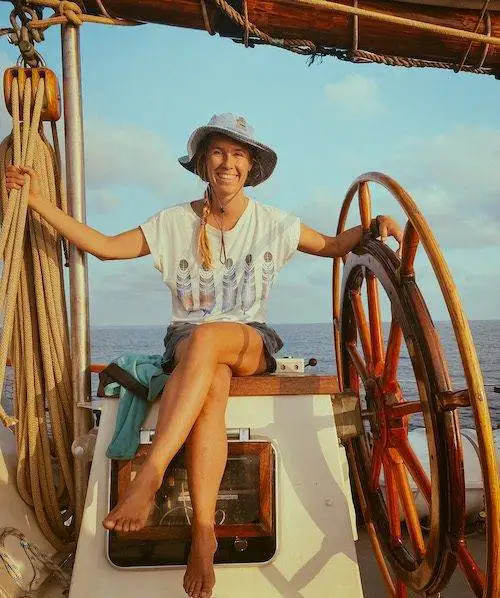 a woman sitting on the steering wheel of a sailboat.