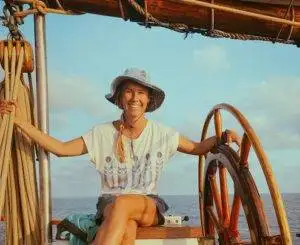 a woman sitting on the steering wheel of a sailboat.