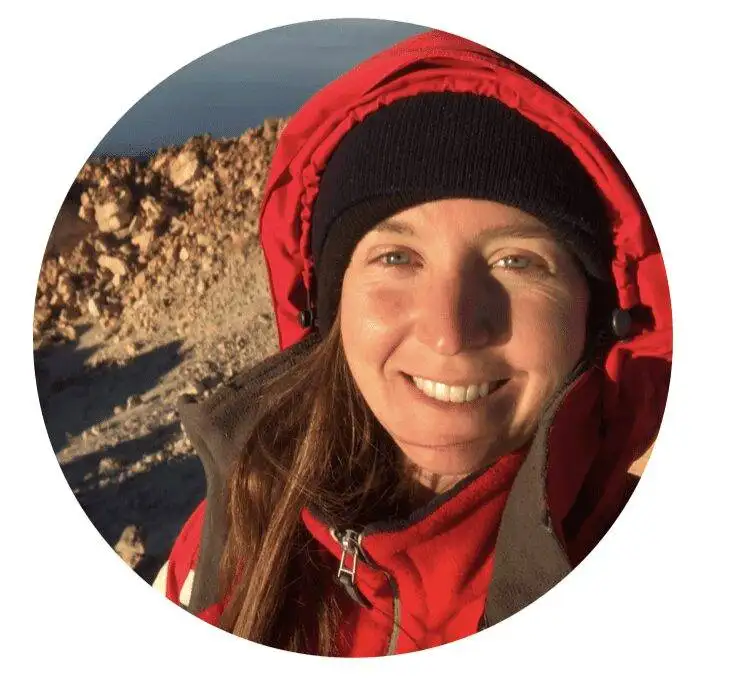 a woman in a red jacket smiling on top of a mountain.