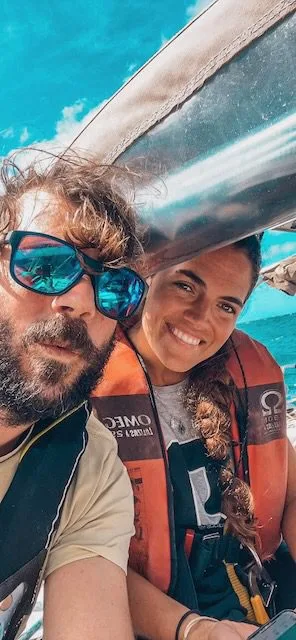 Two people, donning life jackets and sunglasses, are on a boat under the vast blue sky. As they sail towards Cape Verde, the journey unfolds like an adventure from a sunlit postcard.