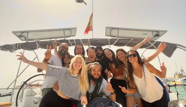 A group of people smiling and posing on a boat with a flag in the background, reveling in their adventure as they navigate the sparkling waters near Cape Verde.