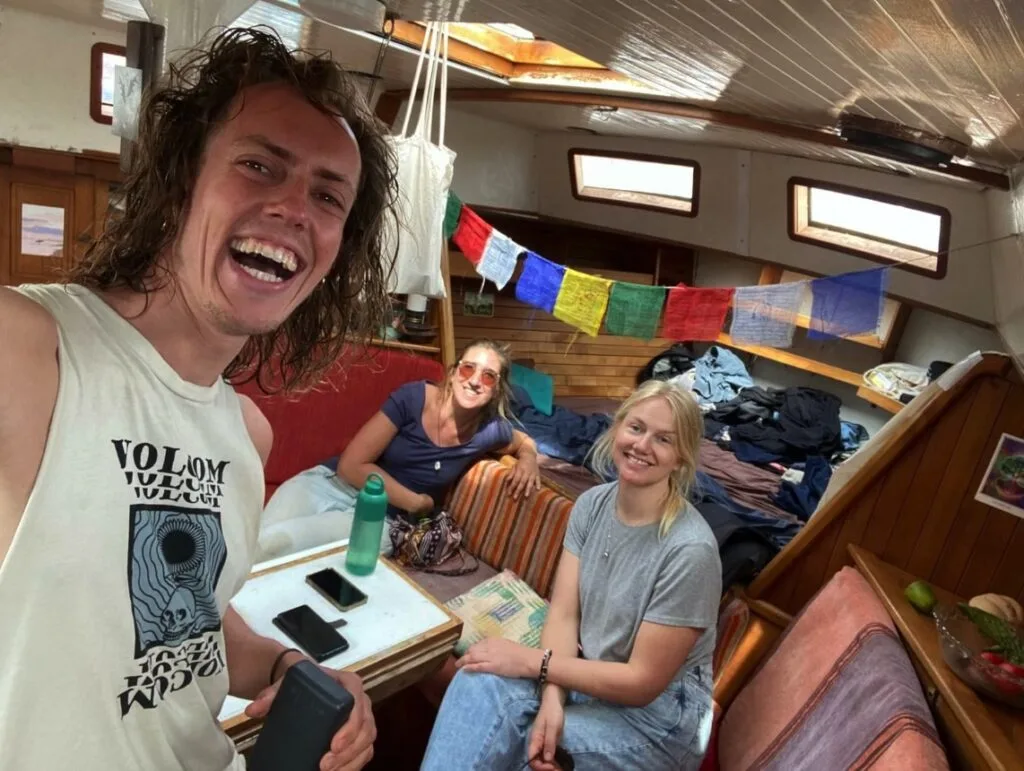 Three ocean nomads beam with joy inside a boat cabin, colorful flags fluttering above, recalling the vibrant spirit of Cabo Verde.
