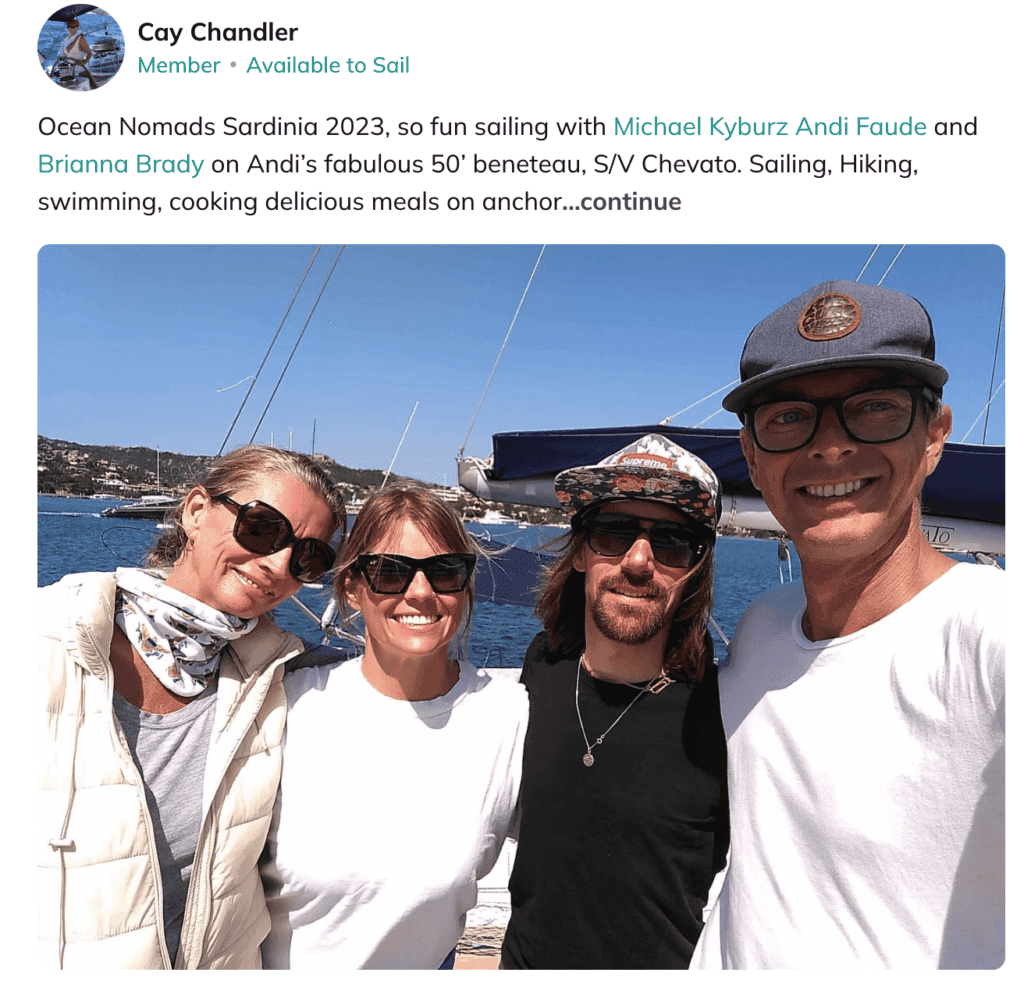 Four people pose and smile in front of a sailboat on a sunny day, enjoying ocean travel with the sea and coastline in the background.