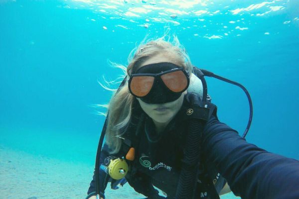 a woman in scuba gear taking a selfie underwater.